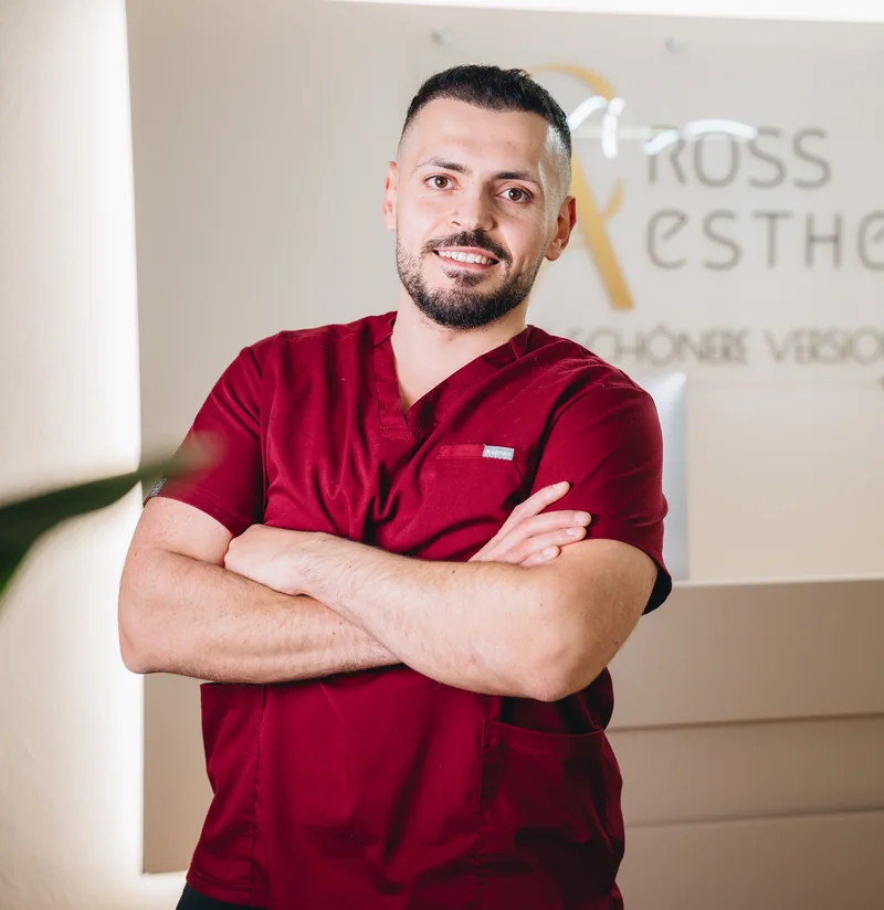 Beshoy Cross mit verschränkten Armen vor dem Logo der Praxis